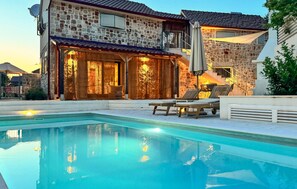A stone building with a pool, lounge chairs, and a covered seating area.