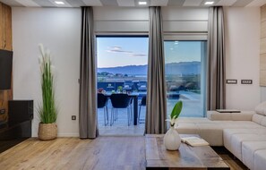 A modern living room with a large window, a sofa, a coffee table, and a dining area with chairs and a table. - Amazing home in Nin with house sea view (Nin)