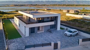 Une maison moderne à deux étages, dotée d’un toit plat, de grandes fenêtres et d’une voiture garée dans l’allée.