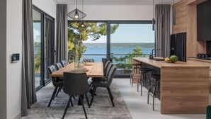 Uma cozinha moderna com uma ilha de madeira, uma área de jantar com uma mesa grande e cadeiras, e vista para um lago através de janelas amplas.
