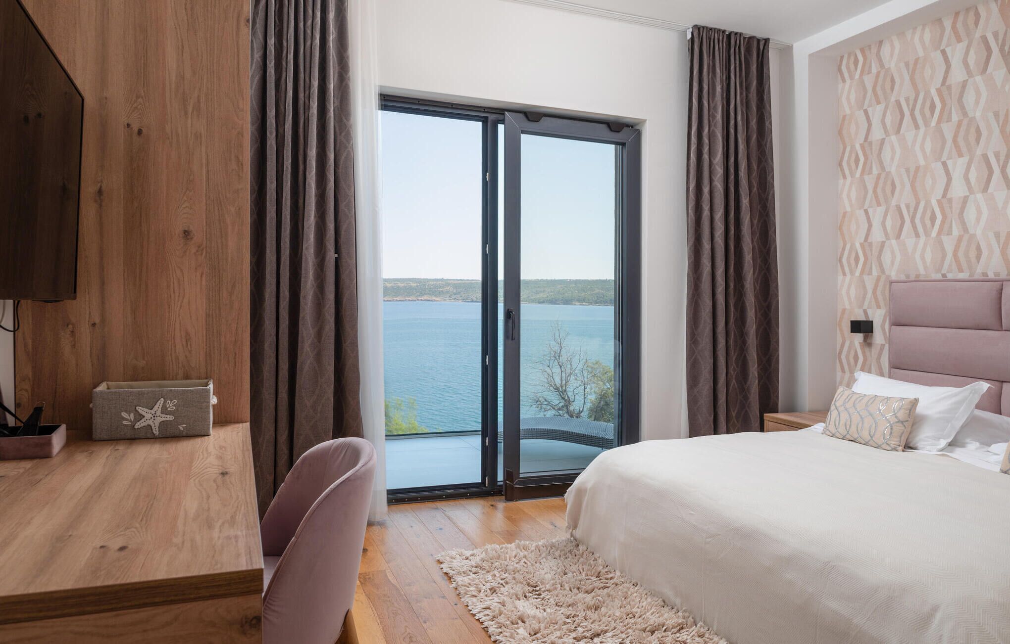 Ein Schlafzimmer mit einem großen Bett, einem Schreibtisch und einem Sessel. Es bietet einen Blick auf ein Gewässer durch eine Schiebetür.