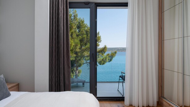 Quarto com uma cama grande, vista para o mar por uma porta de correr e varanda com uma cadeira.