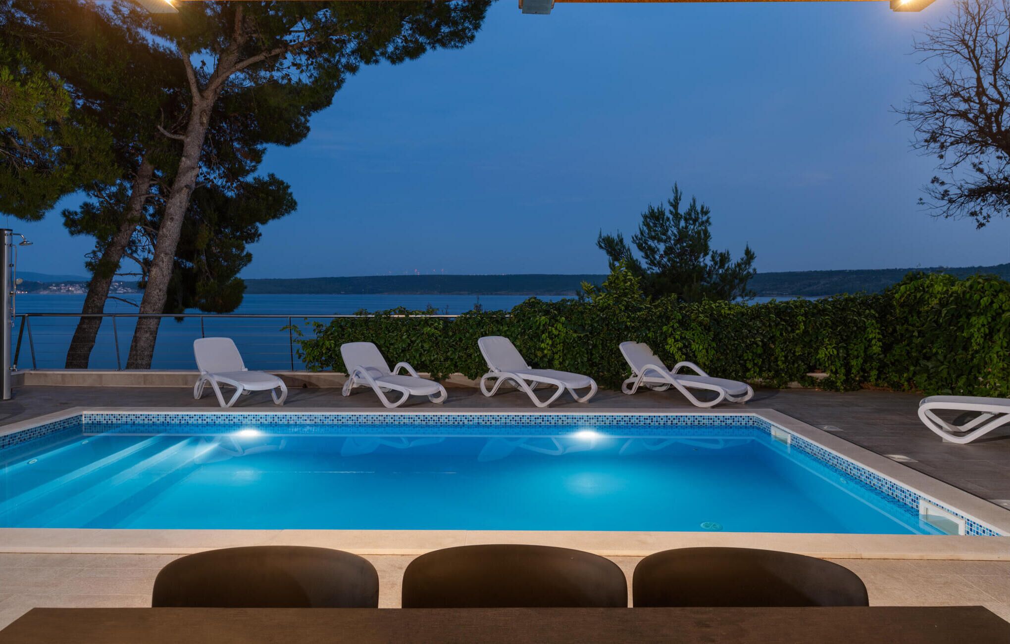 A swimming pool with lounge chairs and a view of the sea at dusk.
