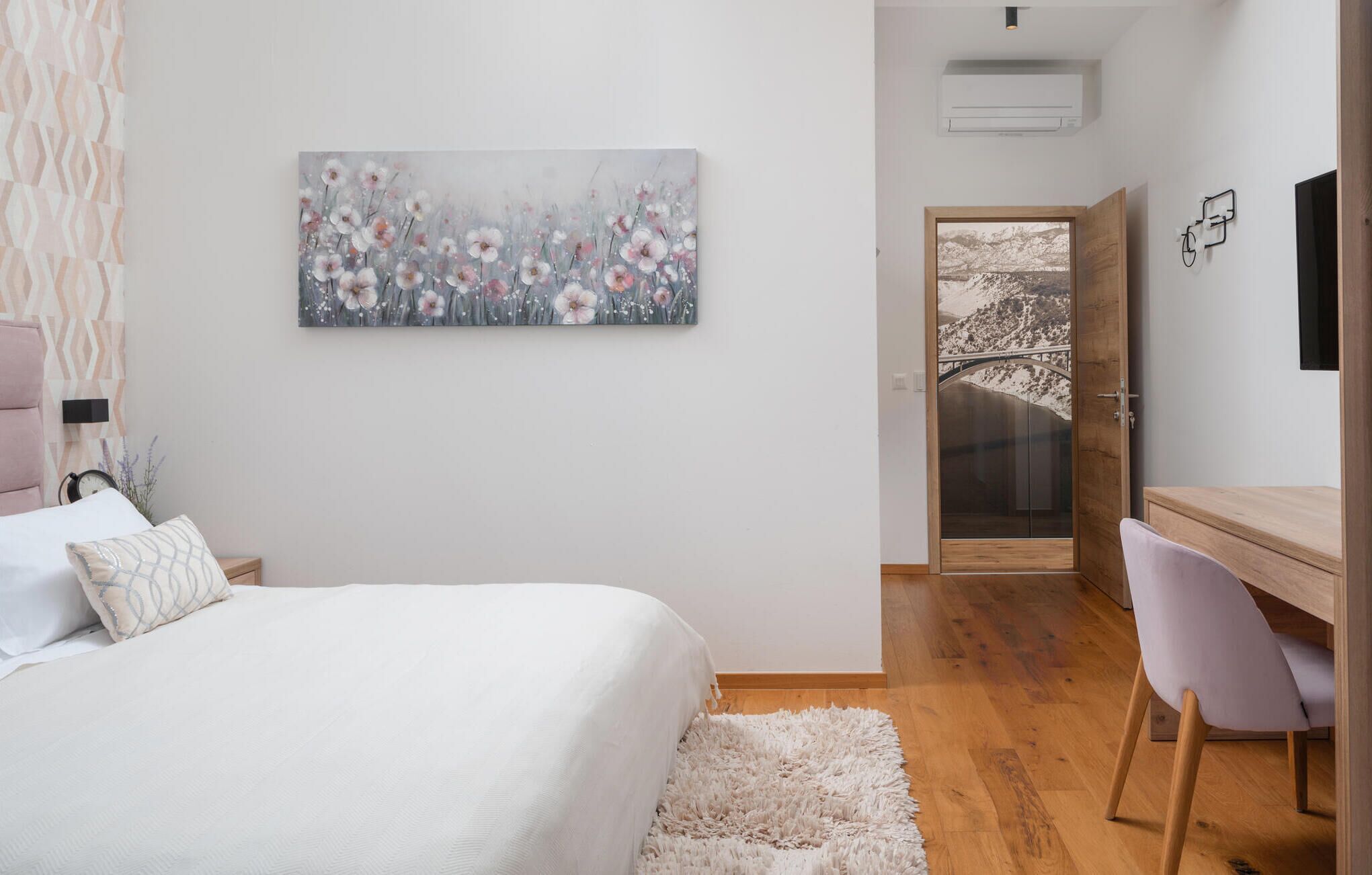 Ein Schlafzimmer mit Bett, Schreibtisch, Stuhl, einem flauschigen Teppich und einem Blumenbild an der Wand.
