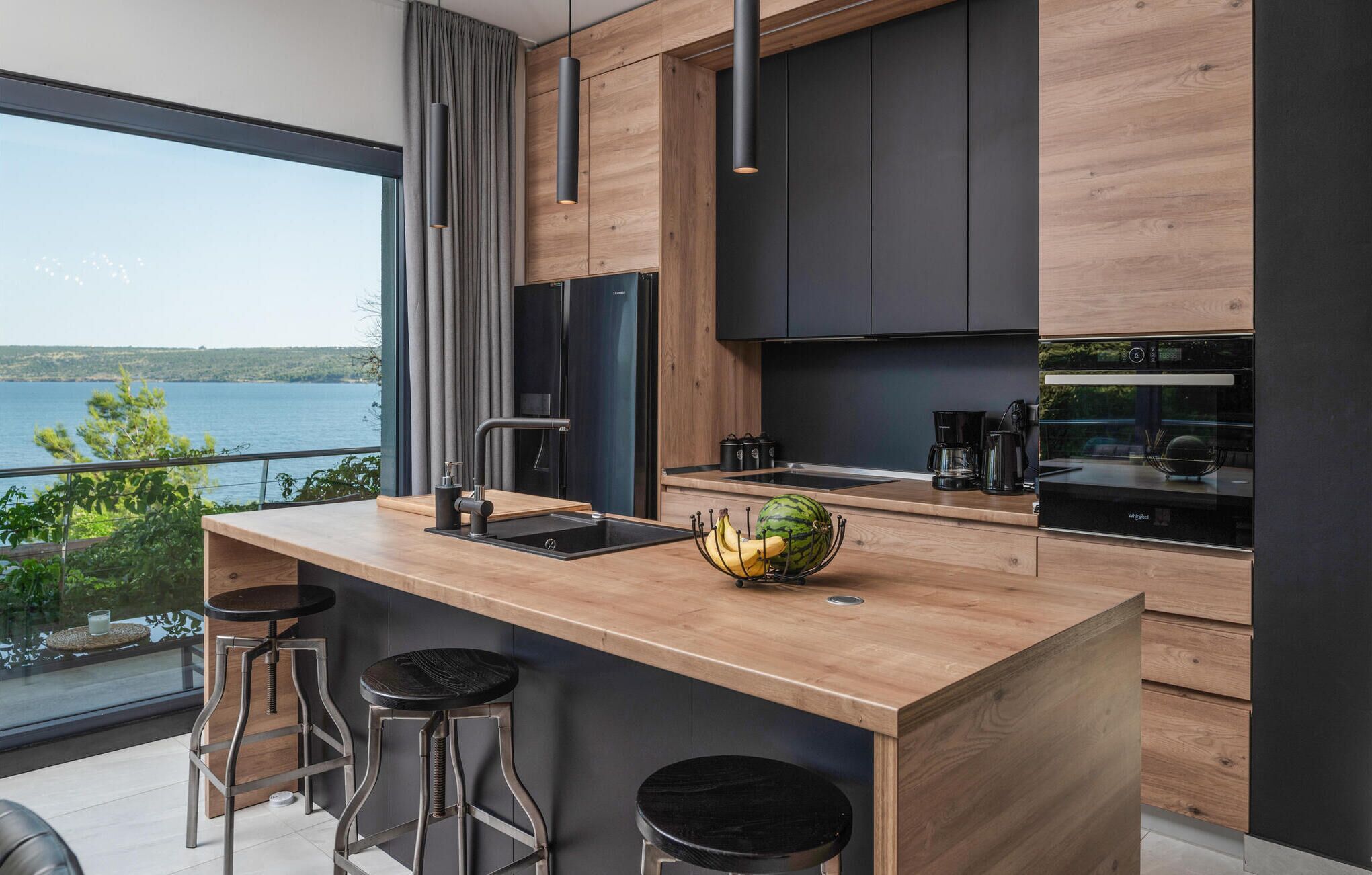 Una cocina moderna con encimera de madera, taburetes negros y vistas al lago.
