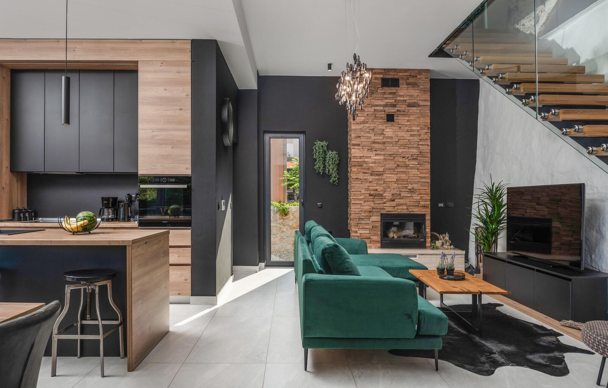 A modern kitchen with dark cabinetry, a wooden island, and a dining area with a green sofa and a coffee table.