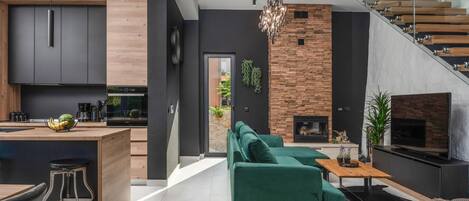 A modern kitchen with dark cabinetry, a wooden island, and a dining area with a green sofa and a coffee table.