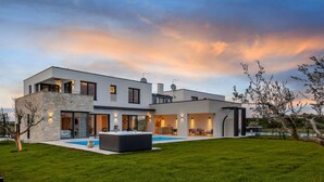 Ein modernes, zweigeschossiges Haus mit Swimmingpool, Steinverkleidung und Außenbeleuchtung.