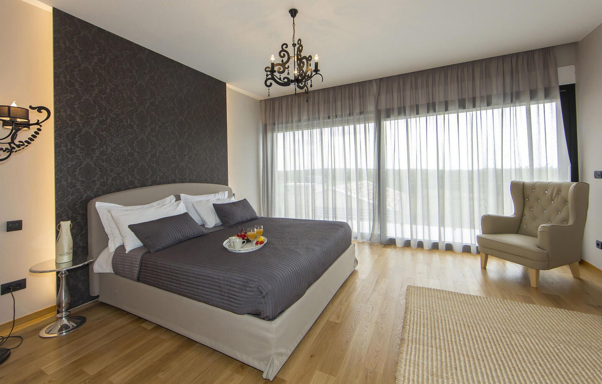 A modern bedroom with a large bed, a side table, a chair, and a chandelier.