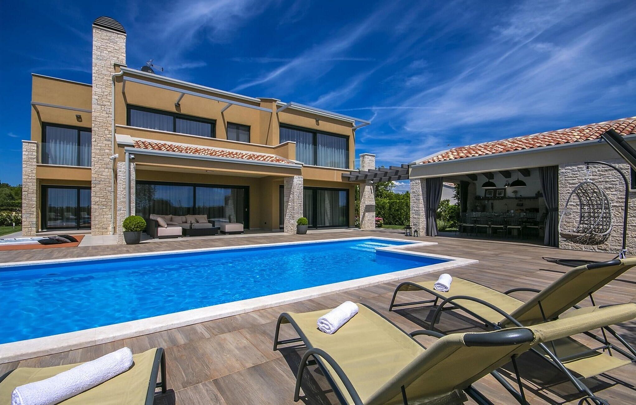 Une maison moderne à deux étages dotée d’une piscine, d’un espace salon extérieur et d’un patio couvert.