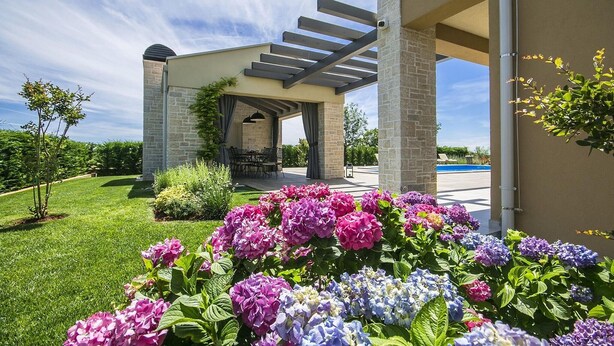 A covered outdoor seating area with stone pillars, a pool, and vibrant flowers in the foreground. - Pet friendly home in Perini (Perini)