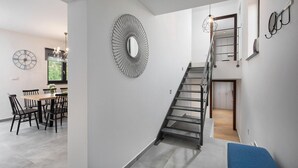 A modern interior with a staircase, a dining area with a wooden table and chairs, and a wall-mounted mirror. - Awesome home in Vinez (Vinez)