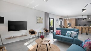 A modern living room with a sofa, a coffee table, and a TV. There is a dining area with a table and chairs, and a kitchen with a stove and cabinets. - Awesome home in Vinez (Vinez)