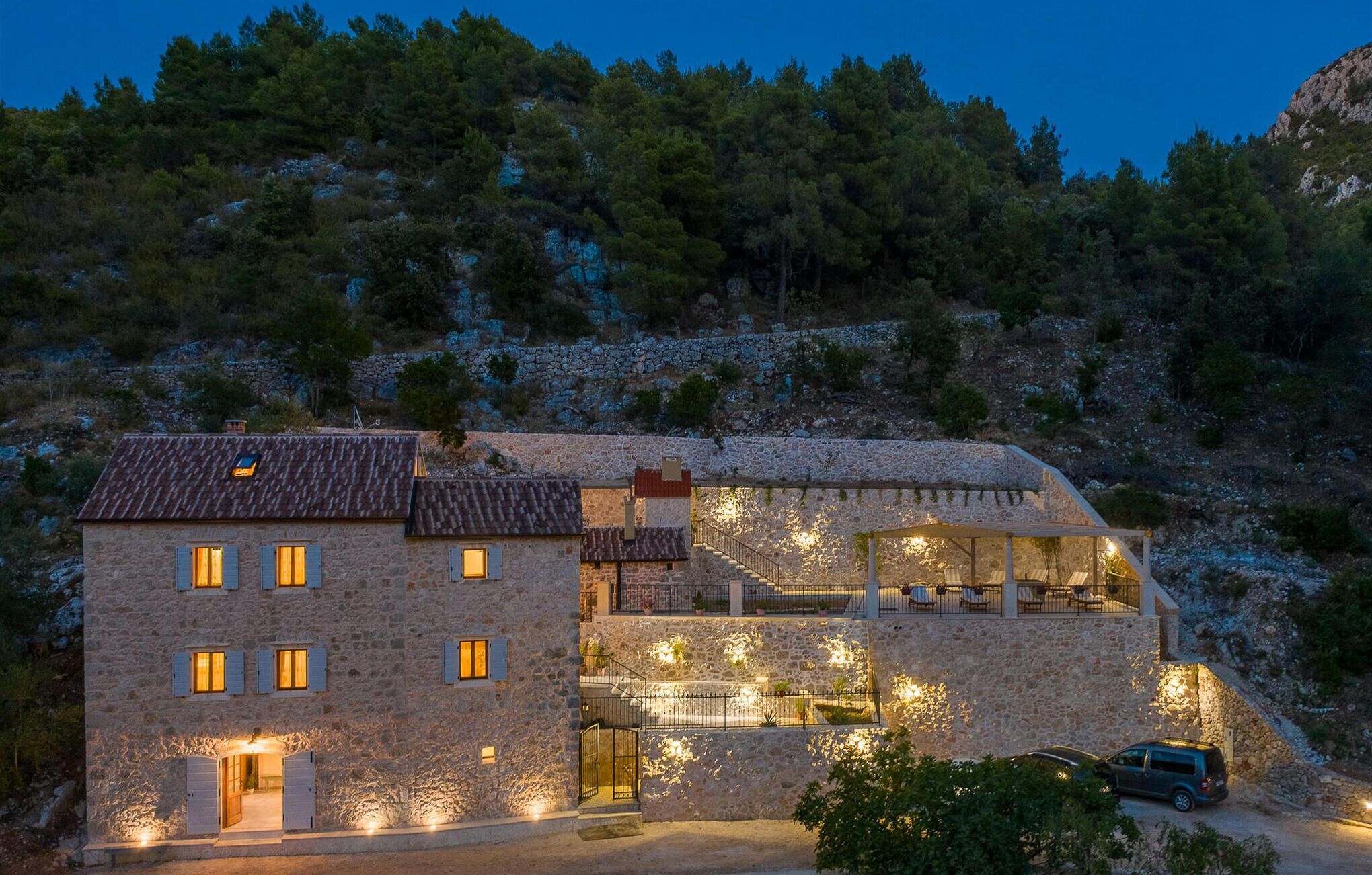 A stone building with multiple windows and a balcony, surrounded by trees and hills.