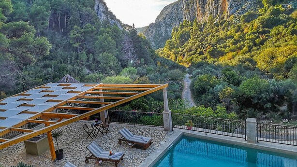 Ein Poolbereich mit Liegestühlen und einer Pergola, eingebettet in eine gebirgige Landschaft.
