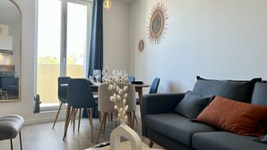 Un salon moderne avec un canapé gris, une table à manger et des chaises, ainsi qu’un vase contenant des fleurs séchées.