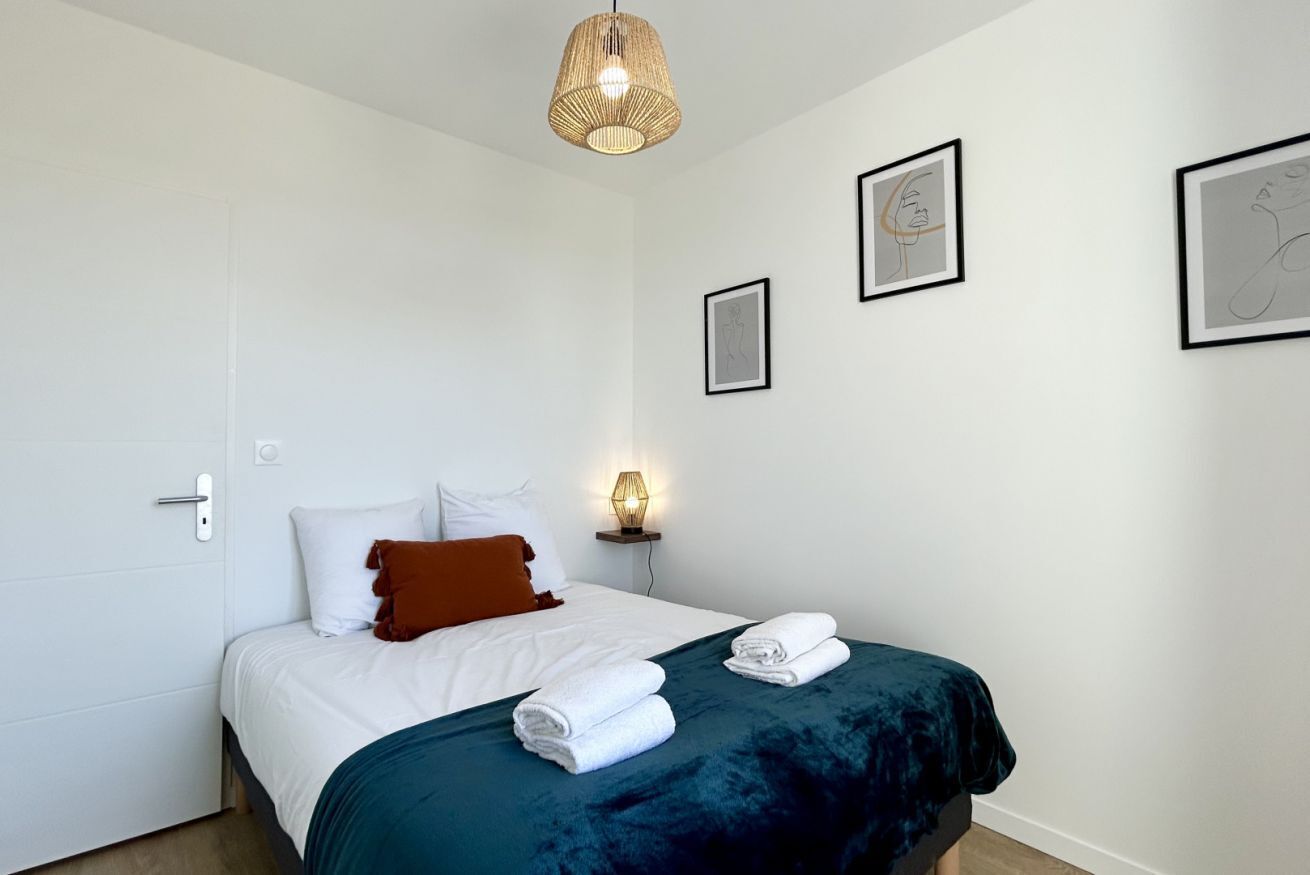 Un dormitorio con una cama, una mesita de noche con una lámpara y cuadros en la pared.