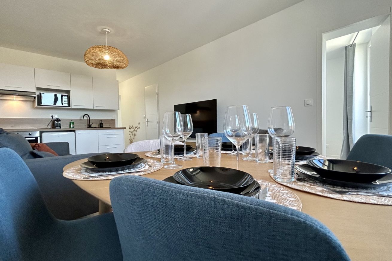 A modern dining area with a wooden table set for four, surrounded by blue upholstered chairs.