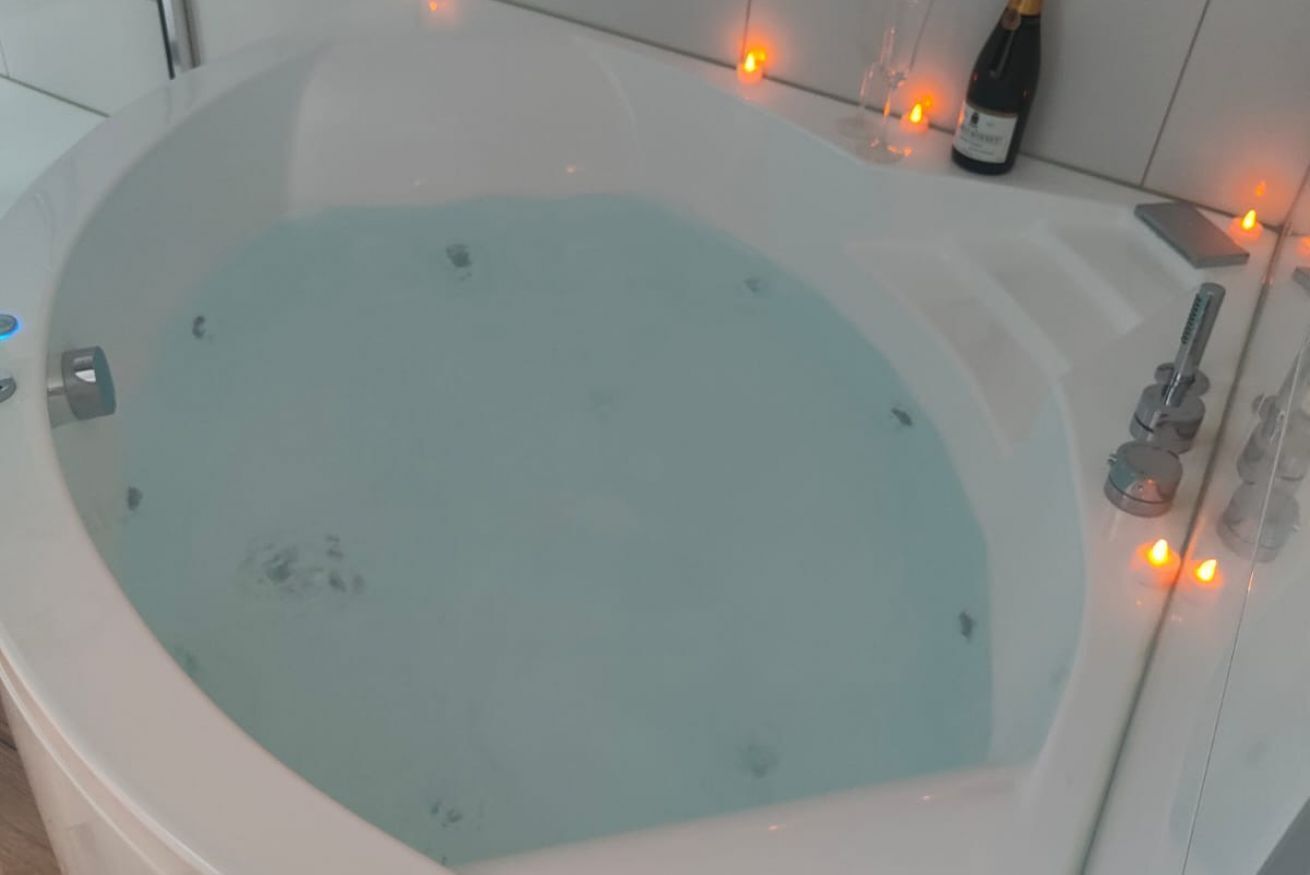 A large, oval-shaped bathtub filled with water, surrounded by a white bathtub with a faucet and a bottle of champagne on the edge.