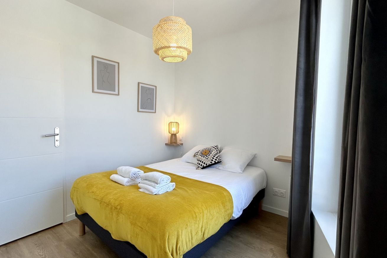 A hotel room with a bed, a bedside lamp, a wall-mounted picture, and a window with curtains.