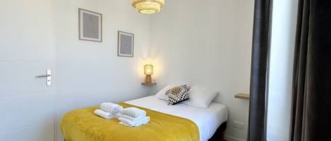 A hotel room with a bed, a bedside lamp, a wall-mounted picture, and a window with curtains.