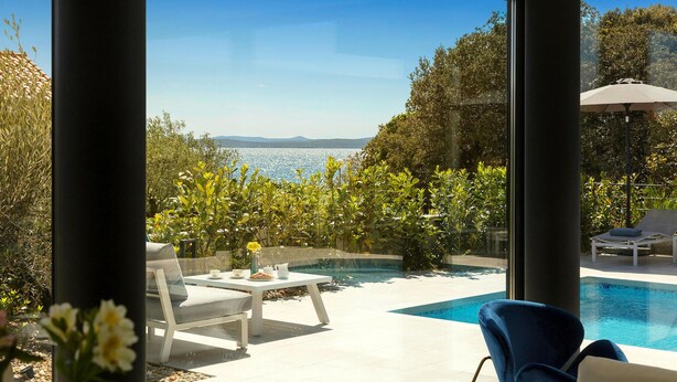Un espace piscine extérieur moderne avec vue sur la mer, comprenant un fauteuil de relaxation et une table agrémentée d’un vase de fleurs.
