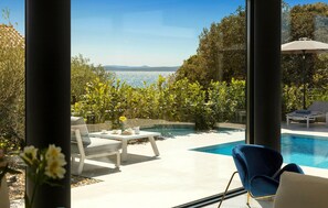 A modern outdoor pool area with a view of the sea, a lounge chair, and a table with a vase of flowers.