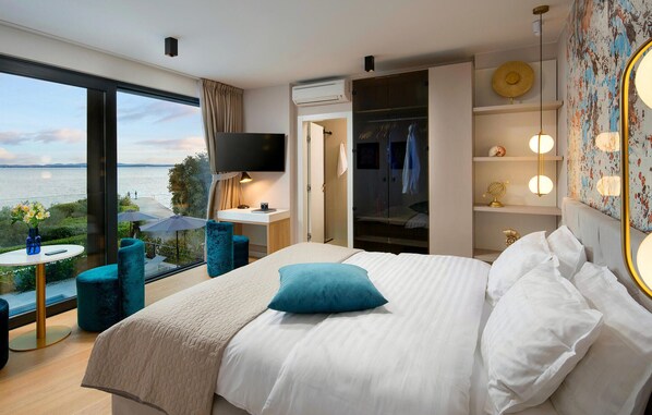 A modern hotel room with a large bed, a desk, a chair, and a view of the sea.