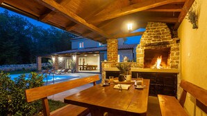 An outdoor patio with a stone fireplace, wooden benches, and a pool area. - 3 bedroom lovely home in Krk (Krk)