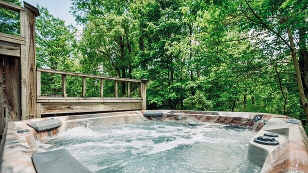 A hot tub surrounded by a wooden deck and lush greenery. - 4 Seasons Wisp - Ski In/Ski Out Townhome with Lake Access, Hot Tub  (McHenry)