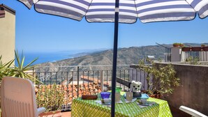 Una terrazza con vista sul mare, un ombrellone a righe e un tavolo con diversi oggetti.
