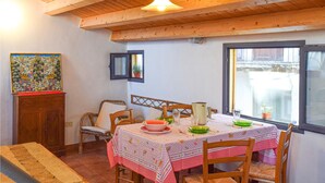 Zona pranzo con tavolo imbandito per quattro persone, sedie in legno, soffitto in legno, una finestra con vista e un quadro appeso al muro.