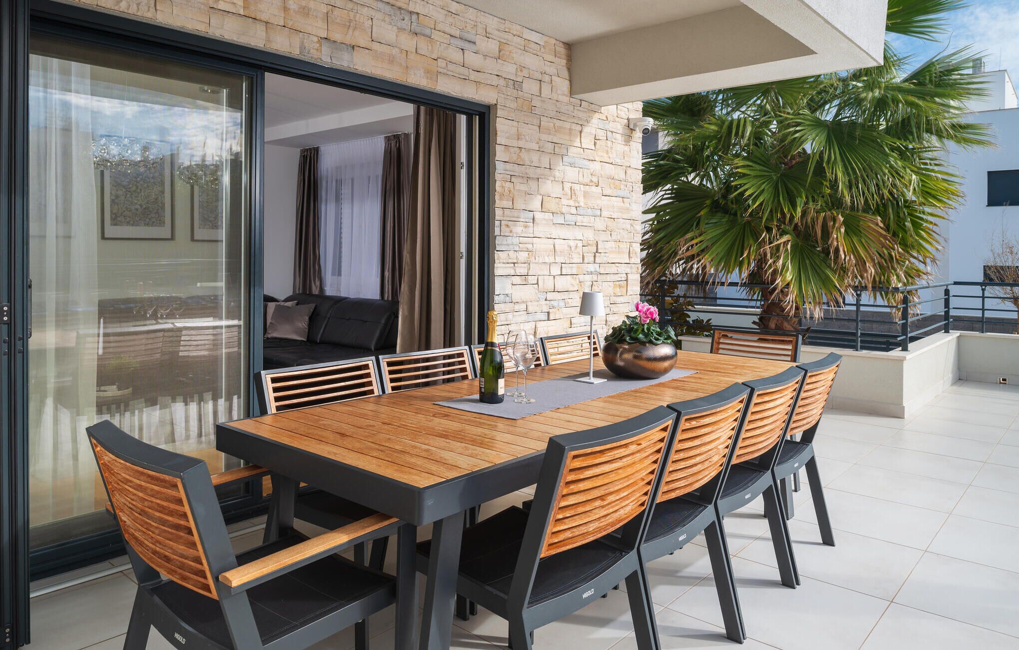 Un coin repas avec une table et des chaises en bois, une bouteille de champagne et un vase à fleurs.
