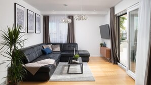 A modern living room with a black leather sofa, a coffee table, and a large window with curtains. - Beautiful home in Privlaka with sauna (Privlaka)