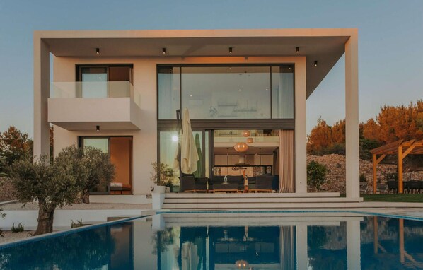 Une maison moderne à deux étages, dotée d’une grande baie vitrée, d’une piscine et d’un espace patio.