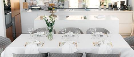 A dining area with a white table set for six, grey chairs, and a vase of white flowers.
