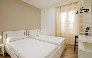 Ein Schlafzimmer mit zwei Einzelbetten, einem Nachttisch, einem Kleiderständer und einem Fenster mit Vorhängen.