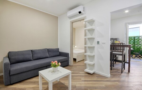 Ein modernes Wohnzimmer mit einem grauen Sofa, einem weißen Couchtisch mit Blumen, einer weißen Regaleinrichtung und einem Essbereich mit einem Holztisch und Stühlen.