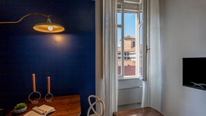 Een kamer met een houten tafel, een hanglamp, uitzicht door een raam en een tv aan de muur.