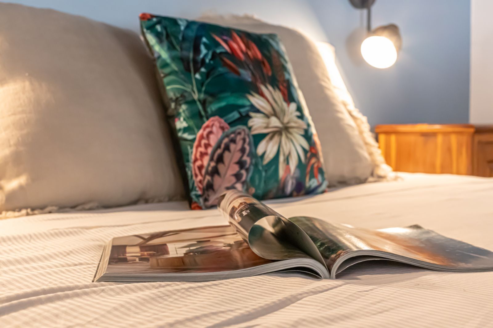 A bed with a pillow, a magazine, and a lamp.