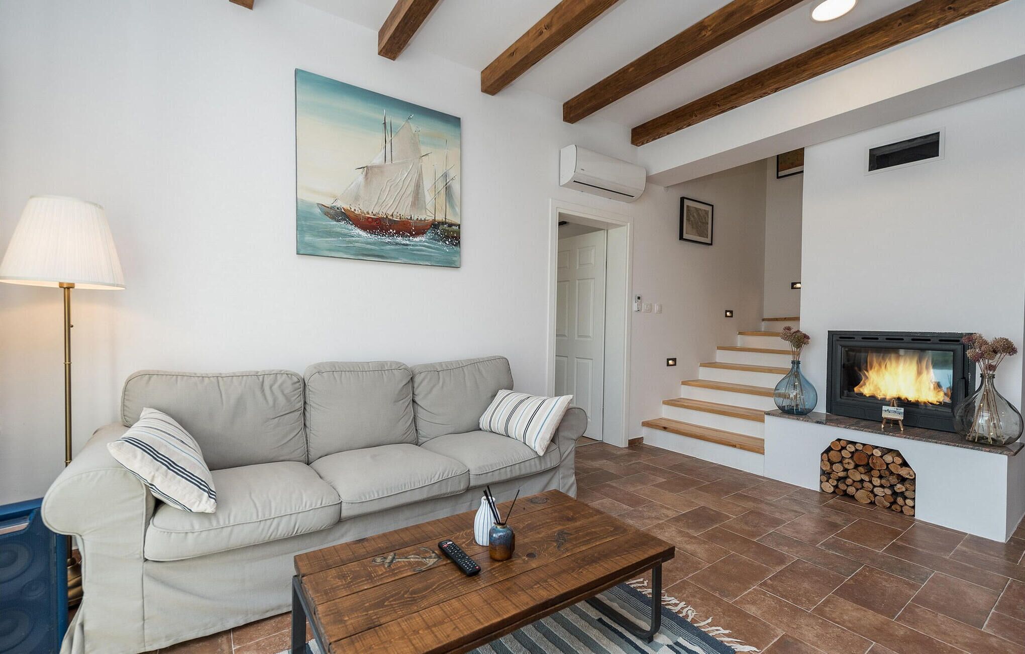 A living room with a sofa, a coffee table, a fireplace, and a painting of a sailboat.