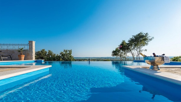 An infinity pool with clear blue water, surrounded by stone walls and potted plants. - Villa Mariva (Carro d'oro) (Vrana)