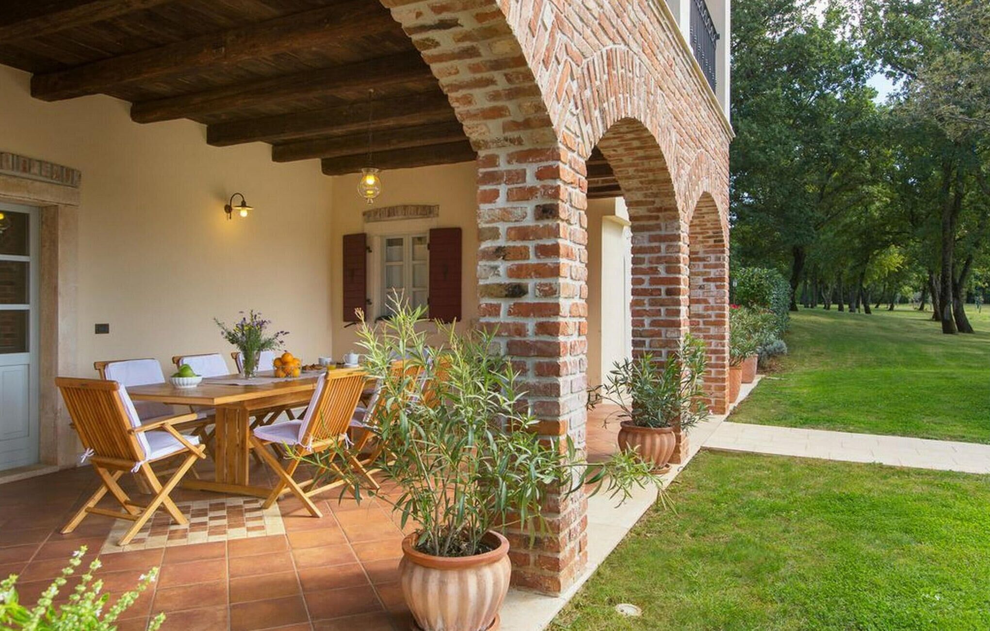 Un patio con una mesa y sillas de madera, rodeado de plantas en macetas.
