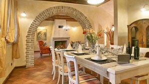 Een eethoek met een lange tafel, witte stoelen en een bakstenen boog.