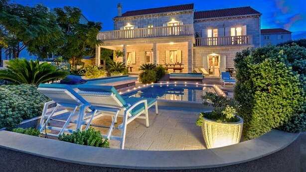 A large, two-story house with a swimming pool, outdoor seating, and well-maintained landscaping.