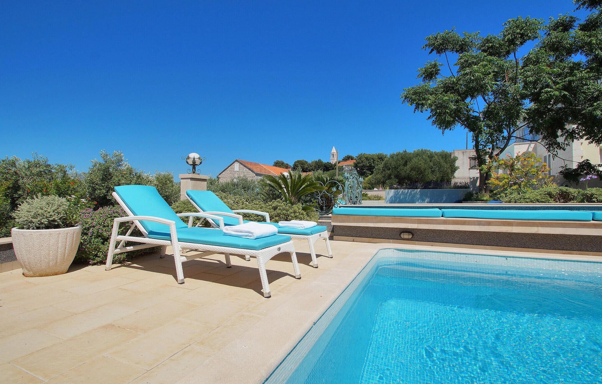 A pool area with two lounge chairs, a decorative fountain, and a clear blue sky.