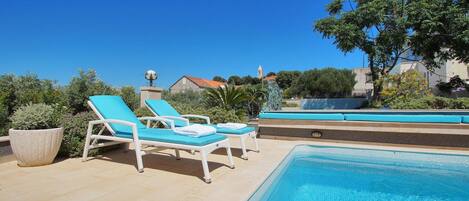 A pool area with two lounge chairs, a decorative fountain, and a clear blue sky.