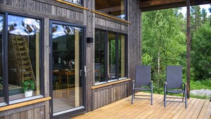 Une terrasse en bois avec deux chaises, de grandes fenêtres et une vue sur les arbres.