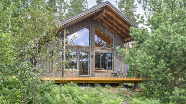 Une cabane en bois dotée de grandes fenêtres, entourée d’une forêt dense.