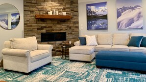 Ein Wohnzimmer mit Kamin aus Stein, zwei Sofas, einem Couchtisch und drei an der Wand hängenden Bildern.